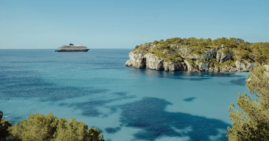 Explora Journeys ship off a Mediterranean cove with turquoise water and limestone cliffs